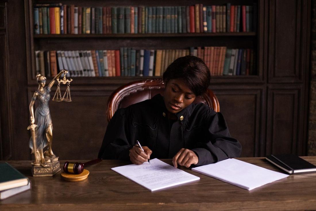 An attorney working at a desk beside law books and a statue of justice